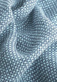 Tessuto intrecciato con un motivo testurizzato nei toni di blu chiaro e blu scuro. Presenta un design a incrocio con fibre morbide e pelose.