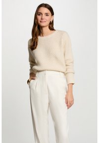 Cremefarbigem Strickpullover mit strukturiertem Muster und langen Ärmeln, kombiniert mit hochtaillierten, weiten weißen Hosen.