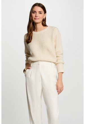 Maglione a maglia color crema con un motivo testurizzato e maniche lunghe, abbinato a pantaloni bianchi a vita alta e a gamba larga.