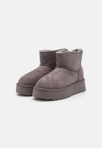 Botas de tobillo de ante gris con un forro suave, que cuentan con una suela de goma gruesa y detalles de costura a lo largo de las costuras.