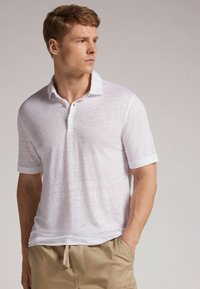 Bílá polokošile s krátkým rukávem vyrobená z lehké, texturované tkaniny, se třemi knoflíky a sklopeným límcem, doplněná béžovými šortkami.