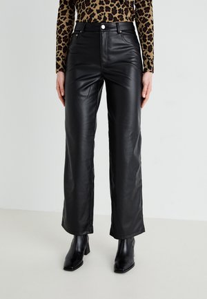 Pantalones anchos de cuero sintético negro con cintura alta, con bolsillos delanteros y cierre de botones metálicos, combinados con botines negros.