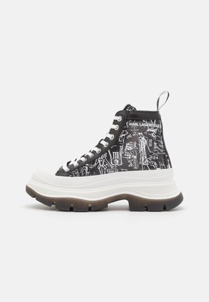 Sneaker alta con un design grafico in bianco e nero, caratterizzata da una suola bianca spessa, lacci neri e una linguetta sul tallone.