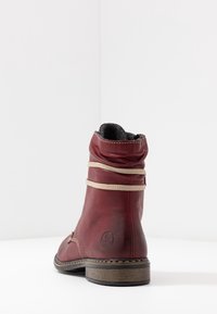 Røde læder ankelstøvler med en tekstureret overflade, beige snørebånd og en rund tå. Har en lav træhælg og kontrasterende syninger.