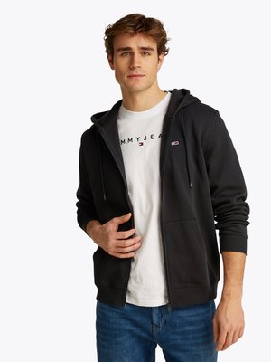 Mørkegrå zip-up hoodie med en frontlomme og hætte, båret over en hvid t-shirt med trykt logo. Afslappet pasform, bomuldsstof, ribbede manchetter.