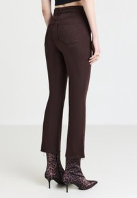 Pantalons marron longueur cheville au design ajusté, avec un léger bord effiloché à l'ourlet. Assortis à des escarpins à bouts pointus imprimé animal.
