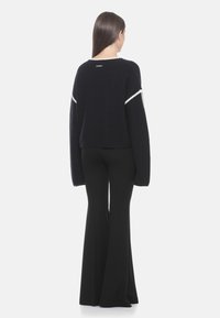 Marineblaue gerippte Pullover mit langen Ärmeln und weißen Akzentnähten, kombiniert mit schwarzen Schlaghosen. Von hinten betrachtet.