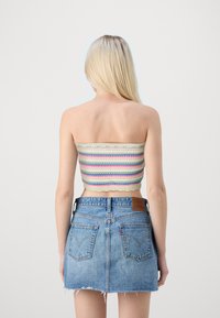 Top a tubino a righe in crema, rosa e verde, abbinato a una gonna di jeans blu chiaro. Il top presenta bordi ondulati, mentre la gonna ha orli sfilacciati.