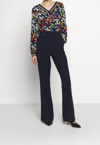 Bluzka z długim rękawem w kolorowy kwiatowy wzór na ciemnym tle, połączona z granatowymi spodniami z dzwonami i czarnymi butami na szpilkach.