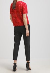 Top in pizzo rosso con maniche corte, caratterizzato da un orlo scallop e un motivo floreale, abbinato a pantaloni neri a sigaretta e sandali con tacco.
