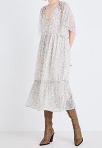 Svetle květinové maxi šaty s výstřihem do V, průhlednými krátkými rukávy a vrstvenou sukní. Vyznačují se jemným vzorem v modré, žluté a krémové barvě.