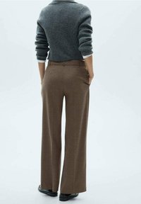 Pantalon large en tartan marron fabriqué à partir d'un tissu texturé, avec une taille haute, des poches et une coupe ajustée, associé à un pull gris.