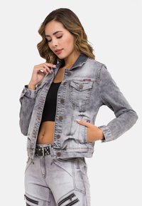 Denimjack in lichtgrijs met knoopsluitingen, twee borstzakken en contrasterende stiksels. Gestyled met een cropped fit en gedragen met bijpassende broek.