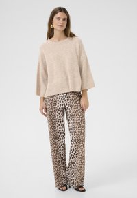 Beige stickad tröja med lös passform ochvida ärmar, parat med byxor med vid ben i leopardmönster i nyanser av brunt och kräm. Svarta sandaler.