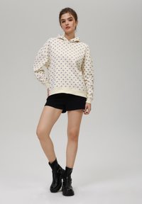 Sudadera crema con pequeño estampado floral en púrpura, puños y cinturilla acanalados, combinada con shorts negros y botines negros.