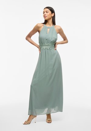 Maxi dress in soft sage green, featuring a halter neckline, keyhole detail, and lace accents at the waist, with flowing fabric and a relaxed fit.