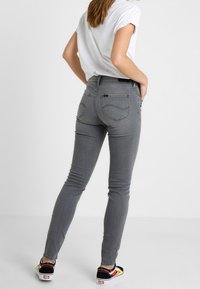 Jeans ajustados grises con cintura alta, que cuentan con un diseño de cinco bolsillos, detalles cosidos y se combinan con zapatillas negras y amarillas.