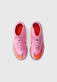 Et par rosa fotballsko med oransje Nike-swoosh-logoer, snøringer bundet og røde interiører på en hvit bakgrunn.