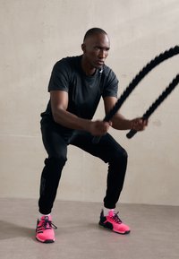 Camiseta atlética negra de manga corta, pantalones negros y zapatillas atléticas de color rosa brillante con detalles verdes. Usando cuerdas de ejercicio gruesas y negras.