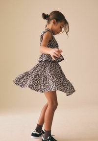 Šaty s leopardím vzorem s vrstvenými volánky, lehká tkanina, bez rukávů, doplněné o černé tenisky a hnědé ponožky.