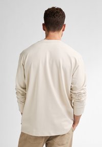 Lange mouwen shirt van lichtbeige katoen, met een ronde hals, ontspannen pasvorm en opgerolde mouwen. Soepele textuur zonder zichtbare patronen.