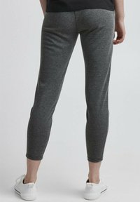 Leggings gris en tissu doux, présentant une coupe fuselée et une longueur jusqu'à la cheville. Portés avec des baskets blanches.
