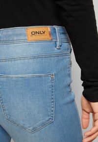 Os jeans azul claro, feitos de denim, apresentam um patch de pele com a marca "ONLY" na cintura, costuras detalhadas e bolsos traseiros.
