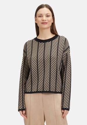 Beige patterned sweater with black zigzag stripes, round neckline, and long sleeves. Paired with light beige wide-leg trousers.