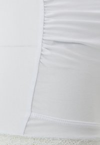 Bielo-tank top so štruktúrovaným ribbed materiálom, zberaným detailom po bokoch a čipkou na okraji. Hladká, jemná tkanina.