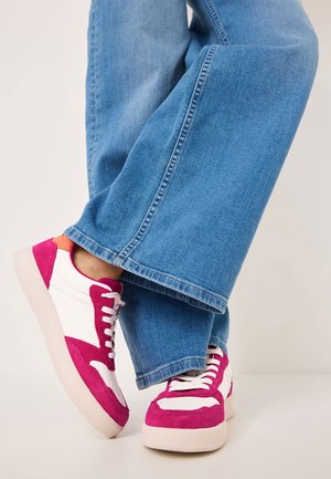 Rosa mocka- och vita läder sneakers med en tjock sula, prydda med rosa snören och oranga detaljer, tillsammans med ljusblå vida jeans.