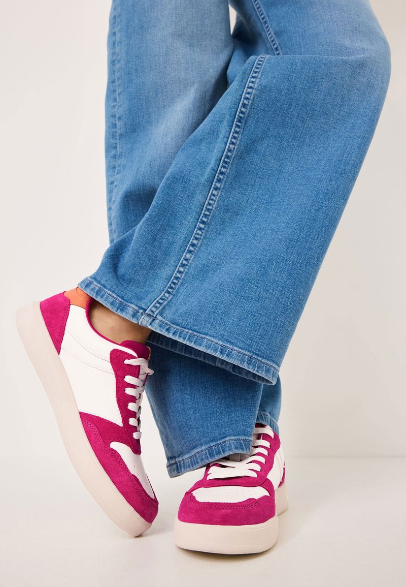 Sneakers in suede rosa e pelle bianca con suola spessa, dotati di lacci rosa e dettagli arancioni, abbinati a jeans a gamba larga di colore azzurro chiaro.