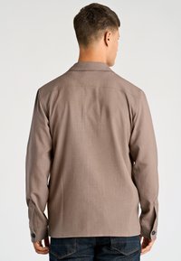 Bruin lang mouw shirt gemaakt van lichtgewicht stof met een gestructureerde kraag, manchetten met een enkele knoop en een gladde textuur.