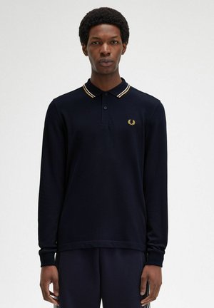 Camisa polo de manga larga en color azul marino con un cuello a rayas en contraste de color dorado y blanco, que presenta un pequeño logo bordado en el pecho.