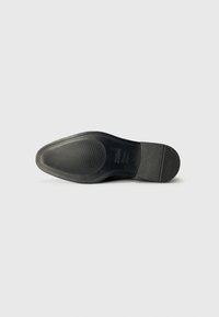 Semelle de chaussure en cuir noir avec un design lisse, présentant une texture nervurée et un bout arrondi. Marque discrète visible près du talon.