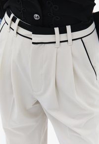 Białe spodnie wykonane z miękkiego materiału, z kantami, czarnym pasem wąskim wykończeniem oraz bocznymi kieszeniami. Zapięcie na srebrny guzik.