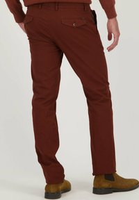 Slim-fit bordeauxrode broek in textuurstof met twee achterzakken en knoopdetail. Gepaard met bruine suede enkelboots.