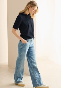 Marinblå kortärmad huvtröja med texturerad tyg, ihop med ljusblå vida jeans, bärs med grå och krämfärgade sneakers.