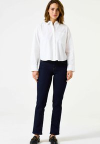 Chemise blanche à manches longues, cropped, associée à un jean en denim bleu foncé. La tenue présente un design et une coupe simples et classiques.