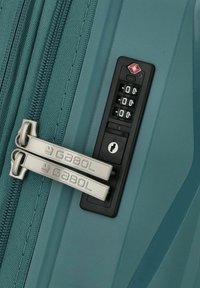 Valigia rigida color teal con cerniera a due vie, marchio Gabol in argento sui tiranti metallici e lucchetto a combinazione approvato dalla TSA.