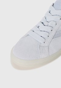 Lys blå semsket sneaker med flate snørebånd, teksturert sidepanel, polstret såle og subtile stikninger langs tåområdet.