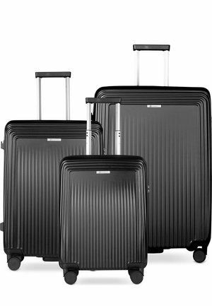 Trois valises rigides noires avec des rainures verticales et des poignées télescopiques étendues, disposées par taille sur un fond blanc.