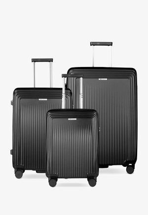Trois valises rigides noires avec des rainures verticales et des poignées télescopiques étendues, disposées par taille sur un fond blanc.