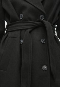 Cappotto in misto lana nero con design doppiopetto, grandi bottoni neri, vita con cintura e texture liscia. Include tasche laterali.