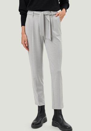 Hellgraue, maßgeschneiderte Hose mit einem Stoffgürtel, der an der Taille gebunden ist, kombiniert mit schwarzen Knöchelstiefeln und einem schwarzen Langarmoberteil.