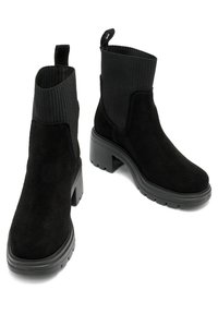 Black suede ankle boots with a ribbed fabric upper, chunky black heel, and loop pull tab. Simple, modern design suitable for various outfits.