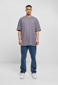 Oversized purple cotton t-shirt with a round neckline and short sleeves, paired with blue denim jeans and white sneakers.
