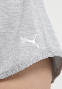 Grå atletiska shorts gjorda av texturerad tyg, med en silverfärgad Puma-logotyp på nederkanten och dekorativ söm längs kanten.
