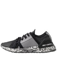 Zapatilla deportiva en negro y gris con una parte superior de tejido texturizado, rayas contrastantes y una suela negra y blanca con un diseño de piel de serpiente.