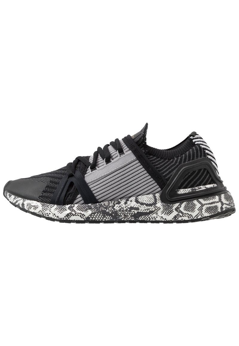 Zapatilla deportiva en negro y gris con una parte superior de tejido texturizado, rayas contrastantes y una suela negra y blanca con un diseño de piel de serpiente.
