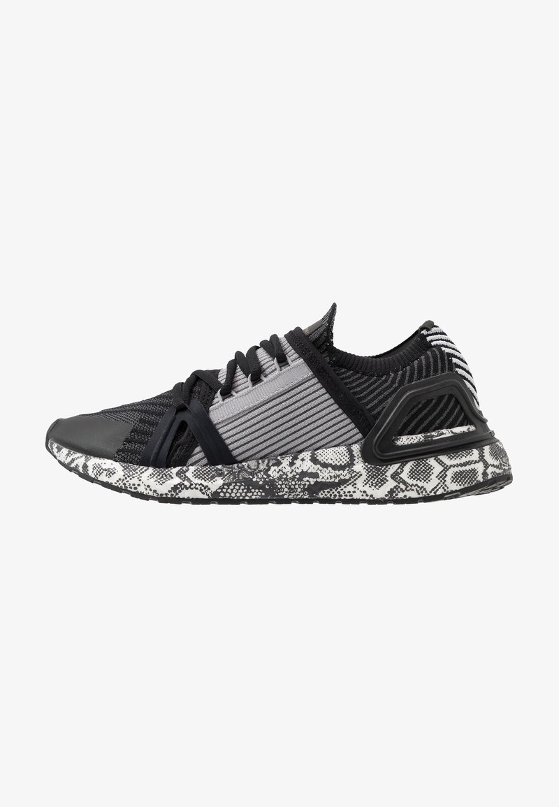 Zapatilla deportiva en negro y gris con una parte superior de tejido texturizado, rayas contrastantes y una suela negra y blanca con un diseño de piel de serpiente.